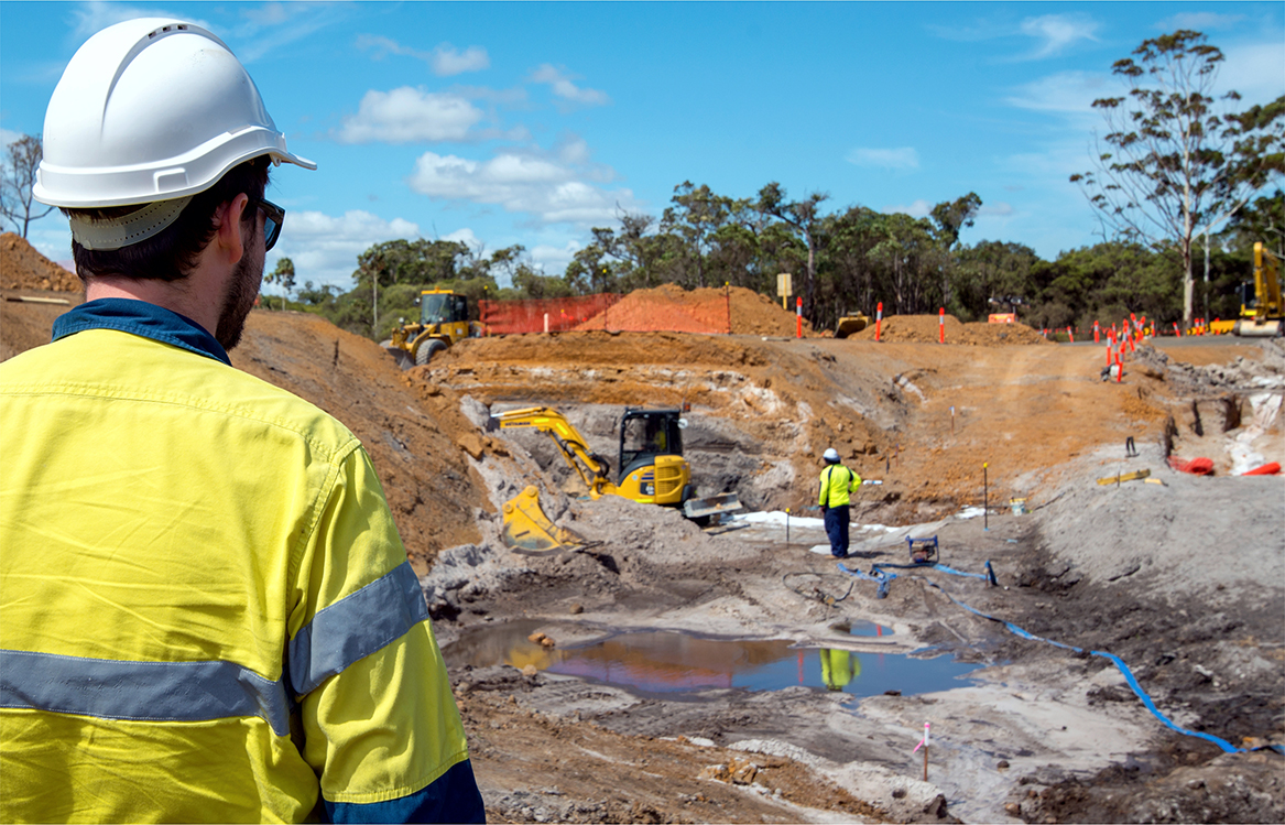 Worker in personal protective equipment looking at a project site with construction vehicles