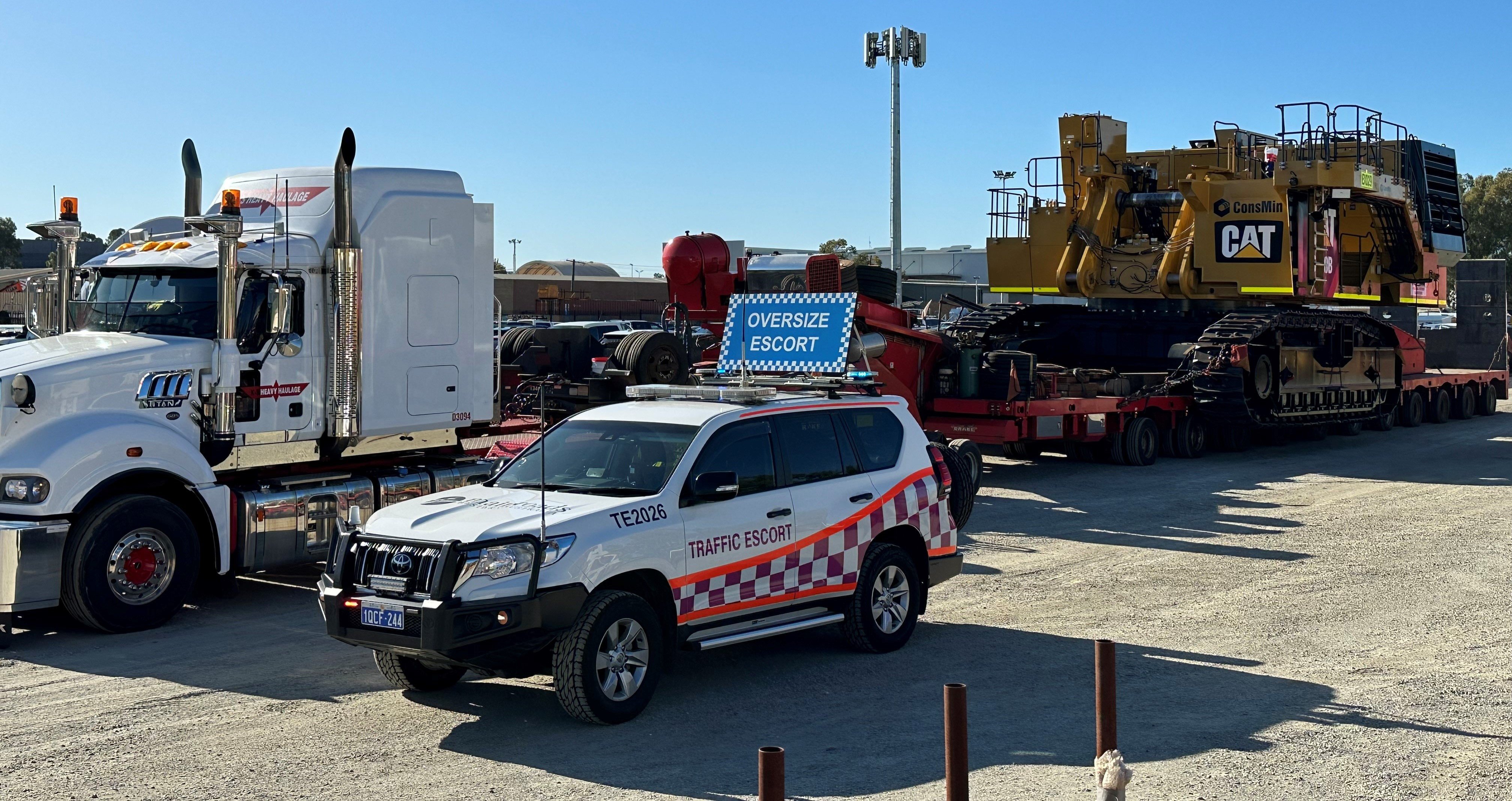 Side view of Traffic Escort Warden Vehicle parked next to an oversize overmass heavy vehicle