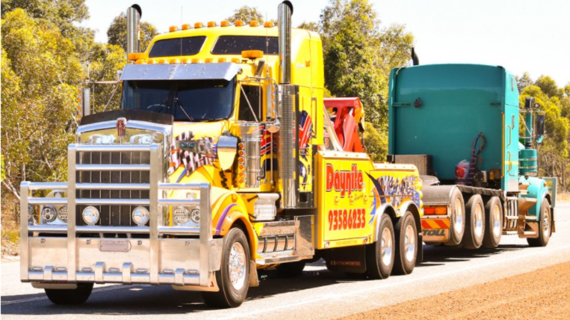 Yellow Heavy Lift Tow Truck towing a teal truck along a road