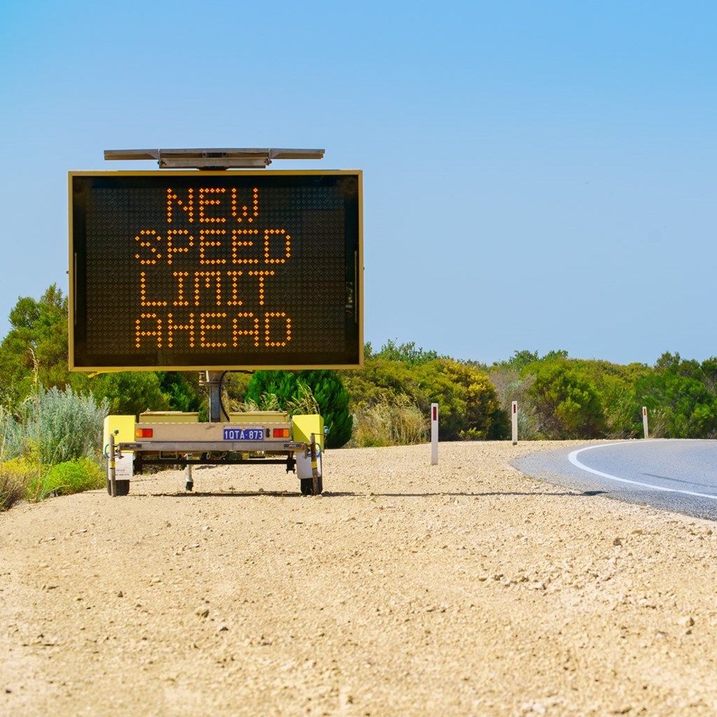 Car travelling on regional road with new speed limit ahead electronic sign