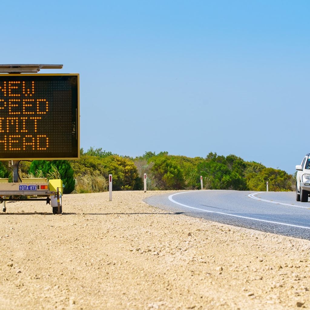 Car travelling on regional road with new speed limit ahead electronic sign