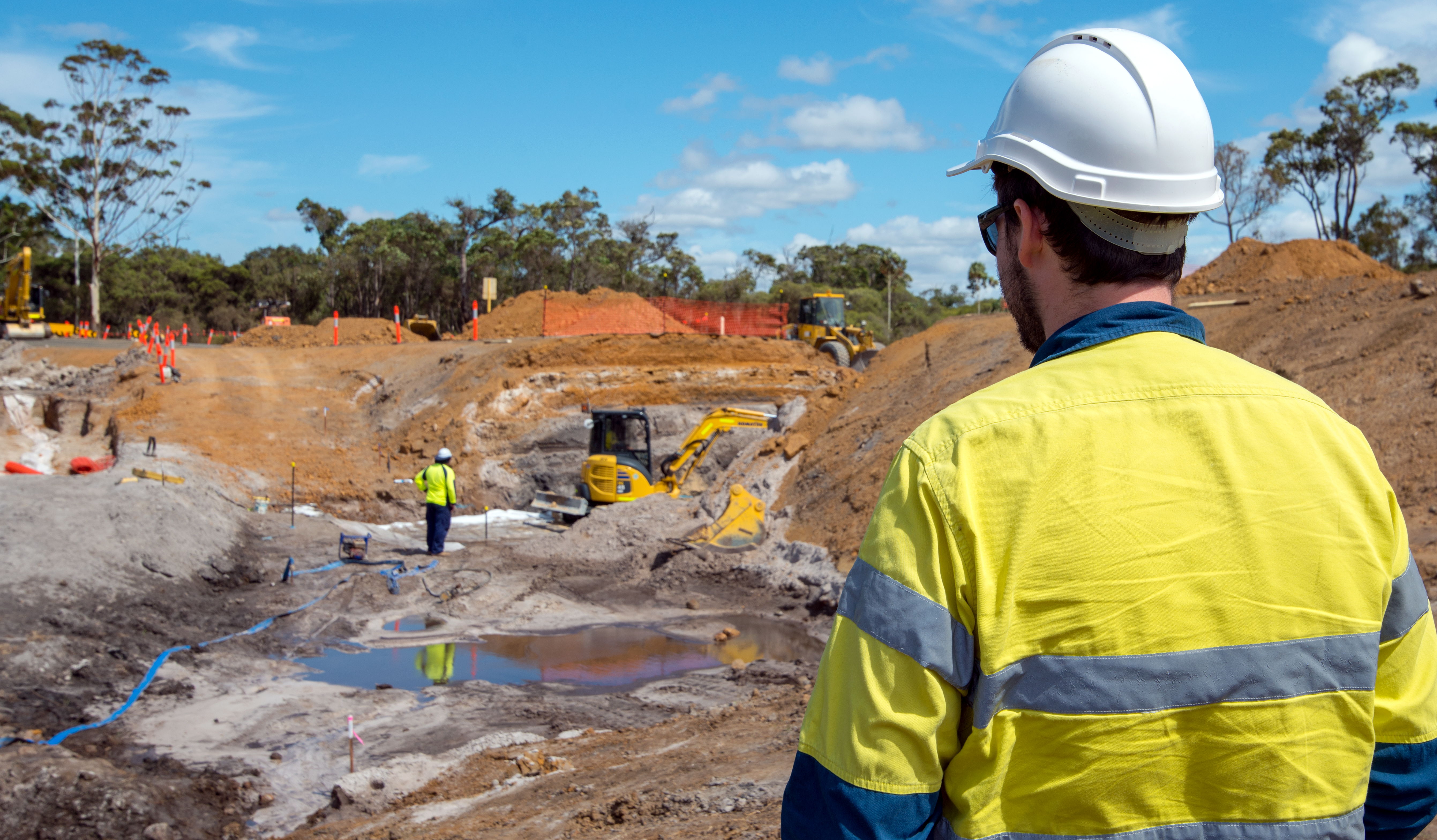 Worker in personal protective equipment looking at a project site with construction vehicles