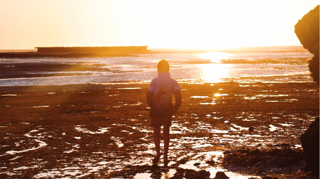 Child standing on the beach watching the sunset