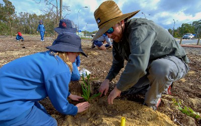 Man helping young kids plant a native tree