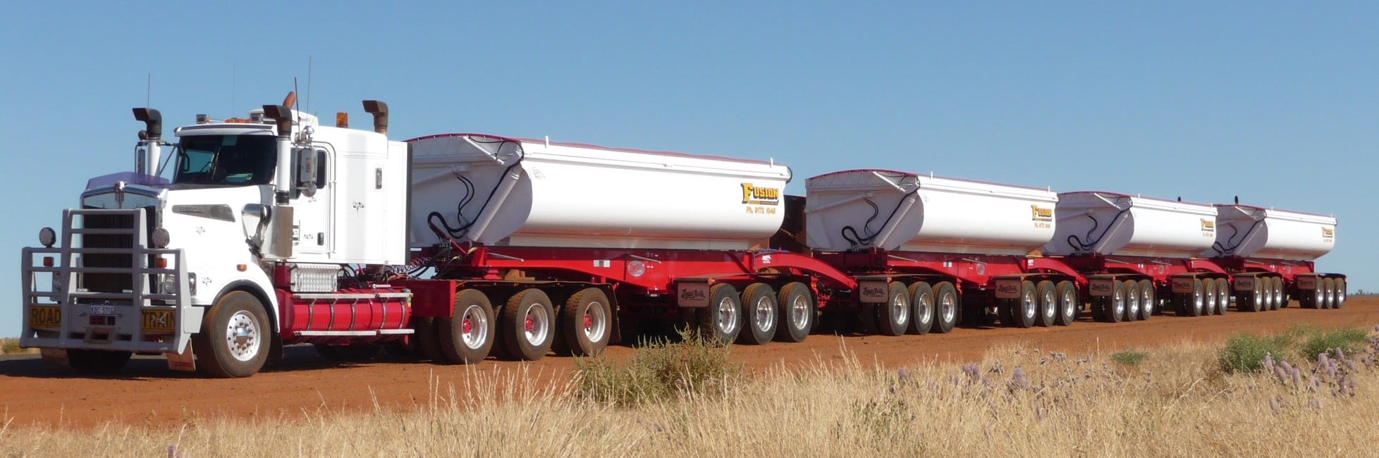 Truck parked on a dirt road with four long trailers attached
