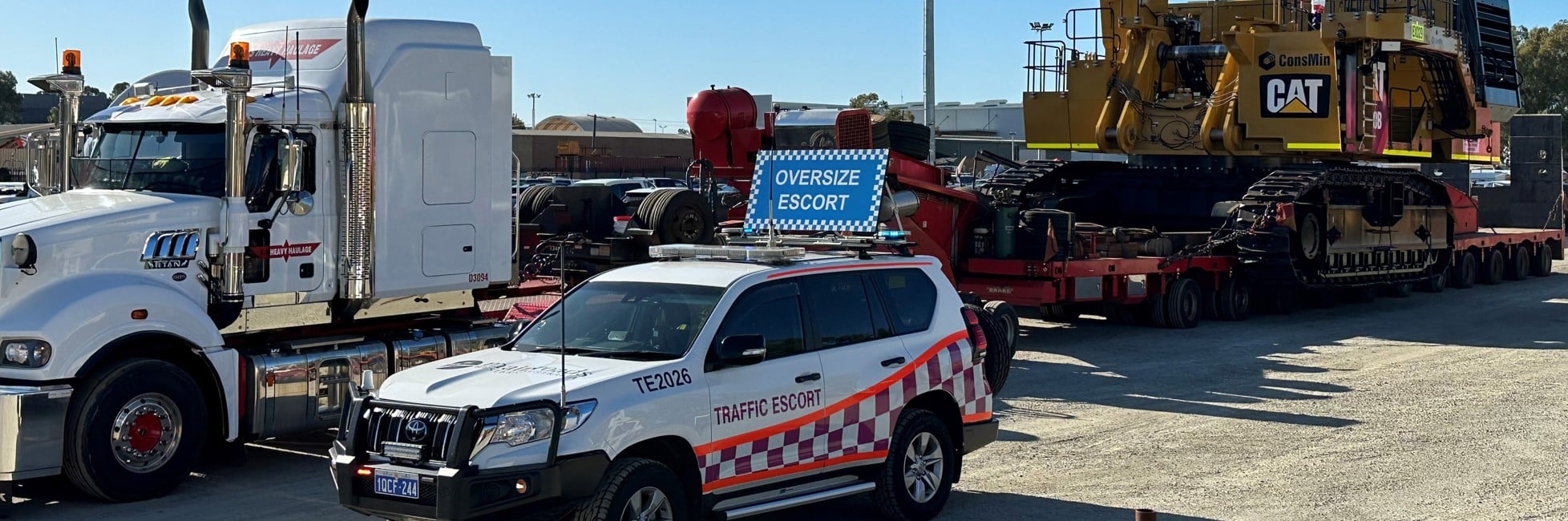 Side view of Traffic Escort Warden Vehicle parked next to an oversize overmass heavy vehicle