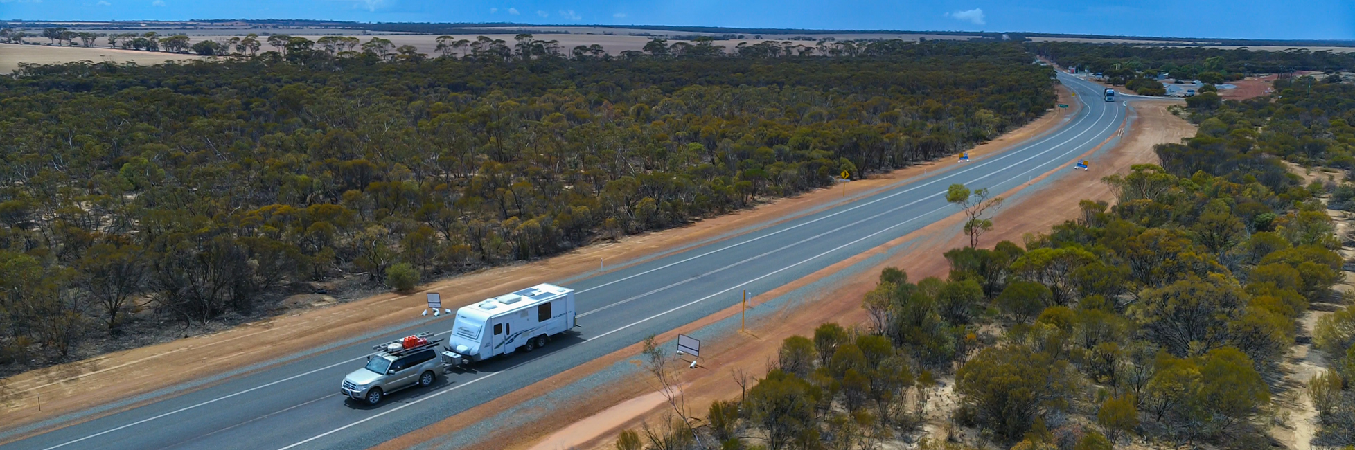 Car towing a caravan travelling along road through trees