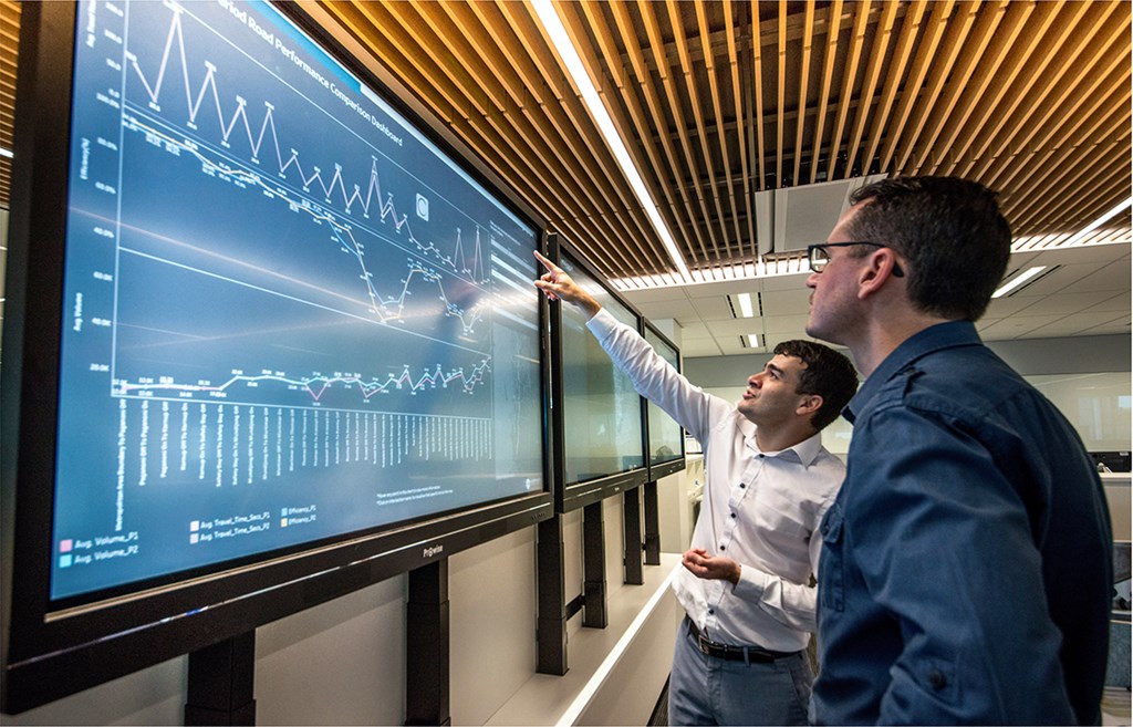 Two workers looking at data on a big screen
