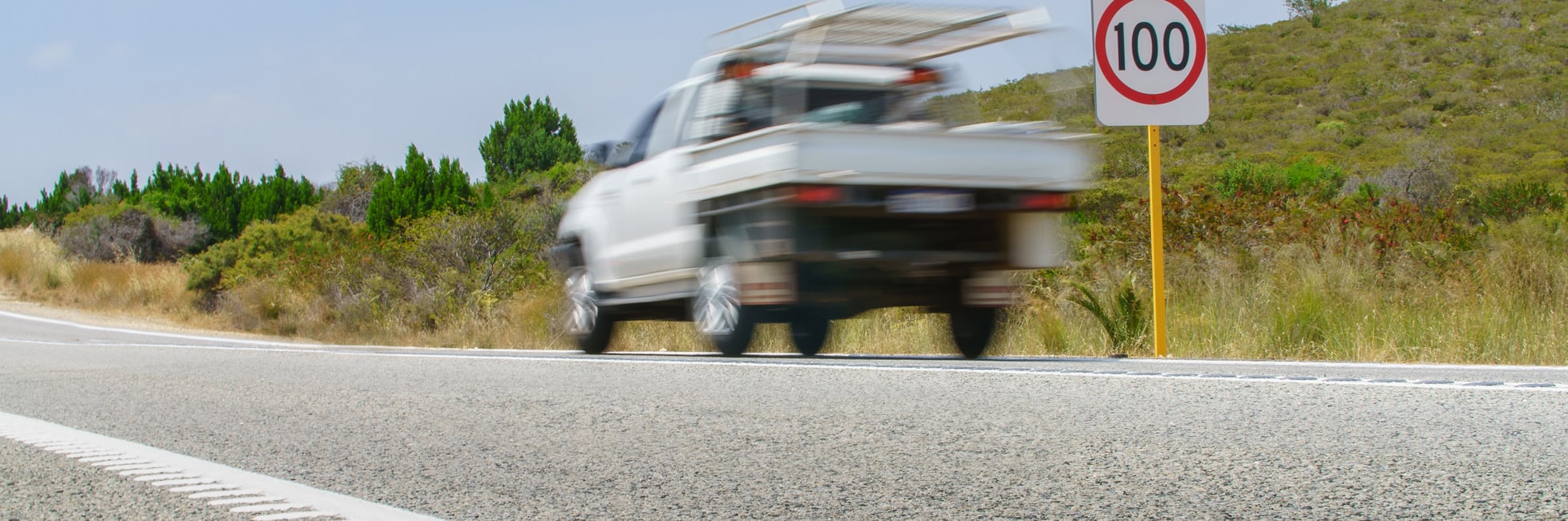 A ute travelling on a road with a 100 km per hour speed sign
